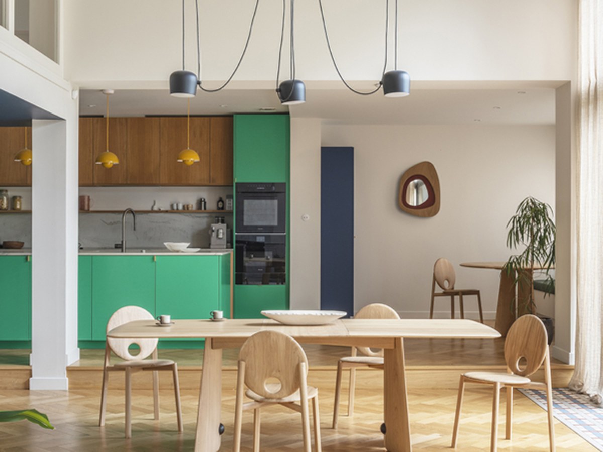 Table et chaises en chêne clair dans une grande pièce à vivre ouverte sur une cuisine verte