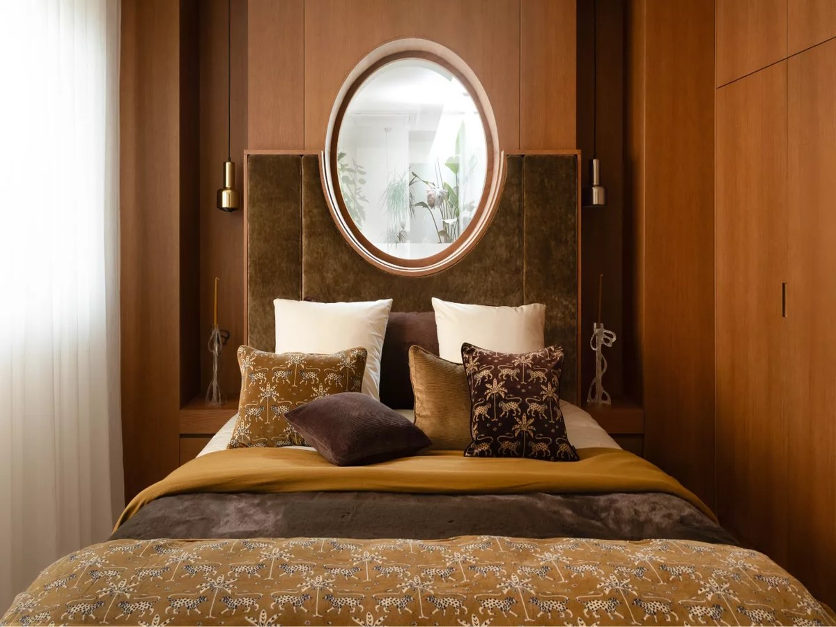 Chambre habillée de bois avec linge de lit en lin ocre et coussins imprimés, ambiance Harmony Haomy