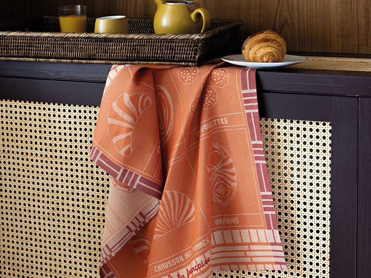 Torchon jacquard terracotta au motif graphique posé sur un buffet en cannage, avec plateau petit-déjeuner