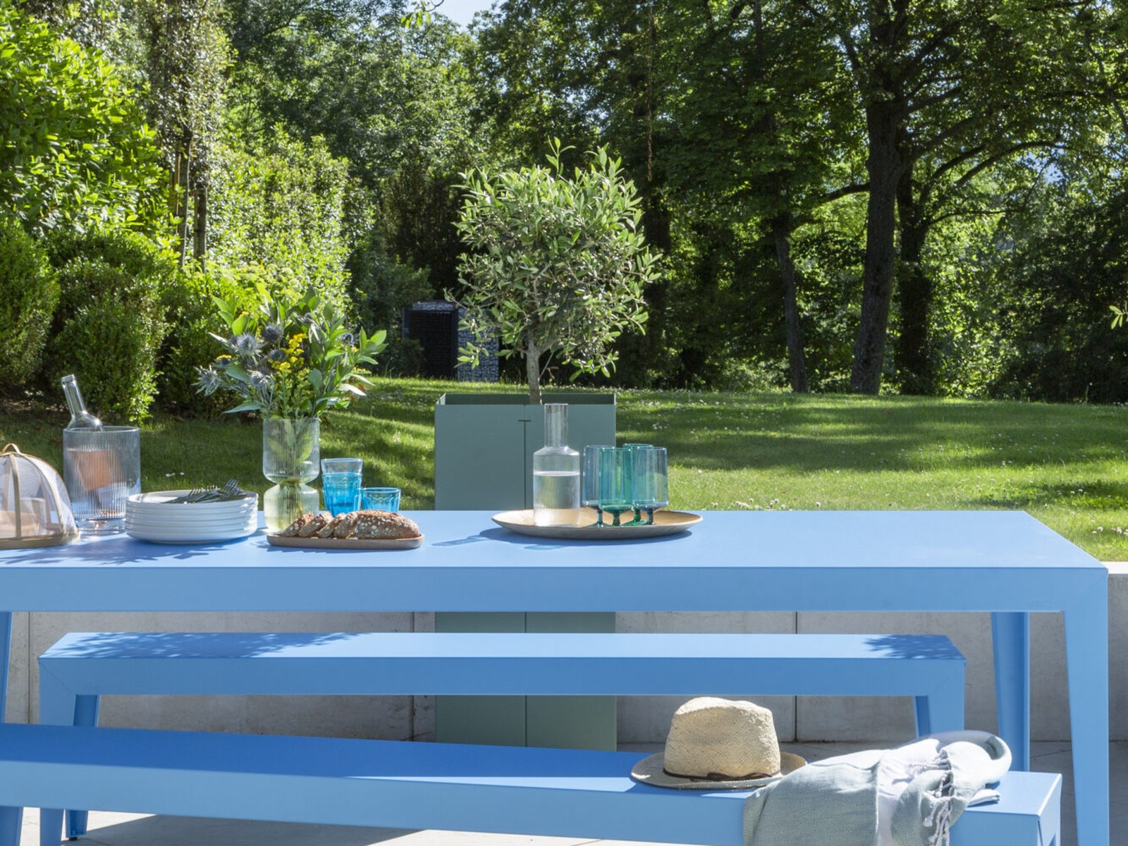Ambiance terrasse Matière Grise : table et bancs d’extérieur en métal bleu dressés dans un jardin