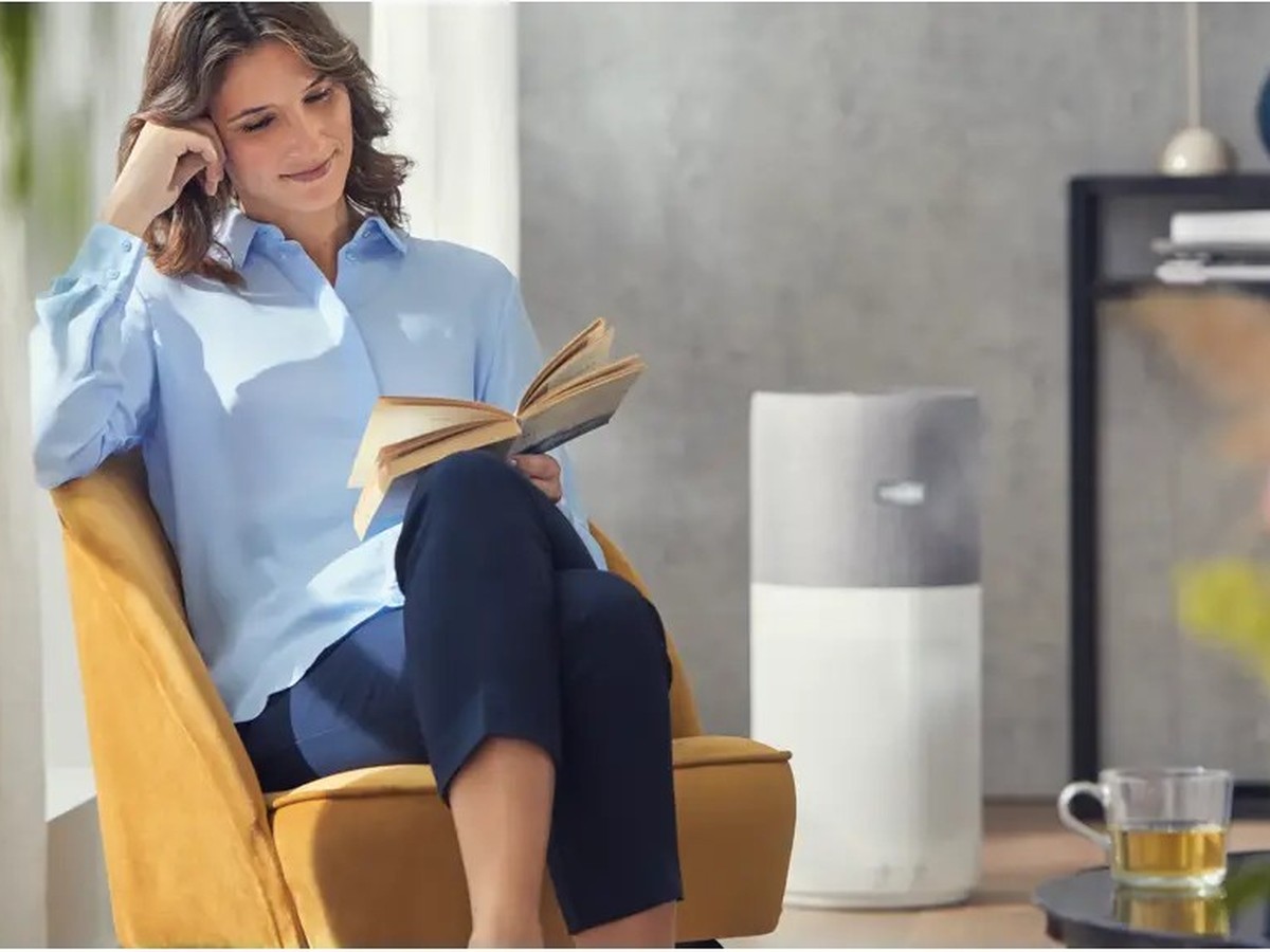 Femme lisant dans un fauteuil moutarde, purificateur d'air Philips Series 3000i en arrière-plan