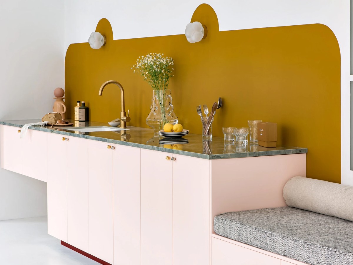 Cuisine Plum Living à façades rose poudré, plan en marbre vert et crédence jaune moutarde